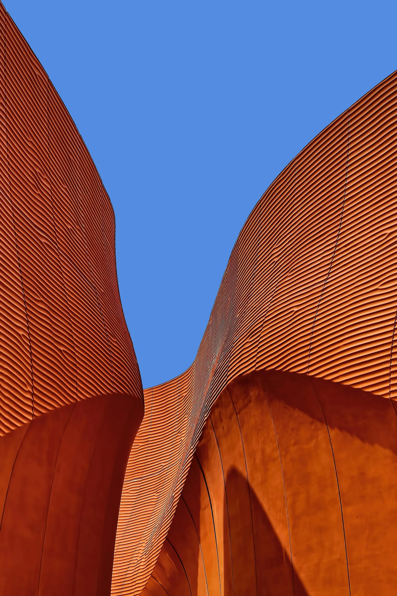 Sweeping curved facade of ribbed terracotta against a blue sky