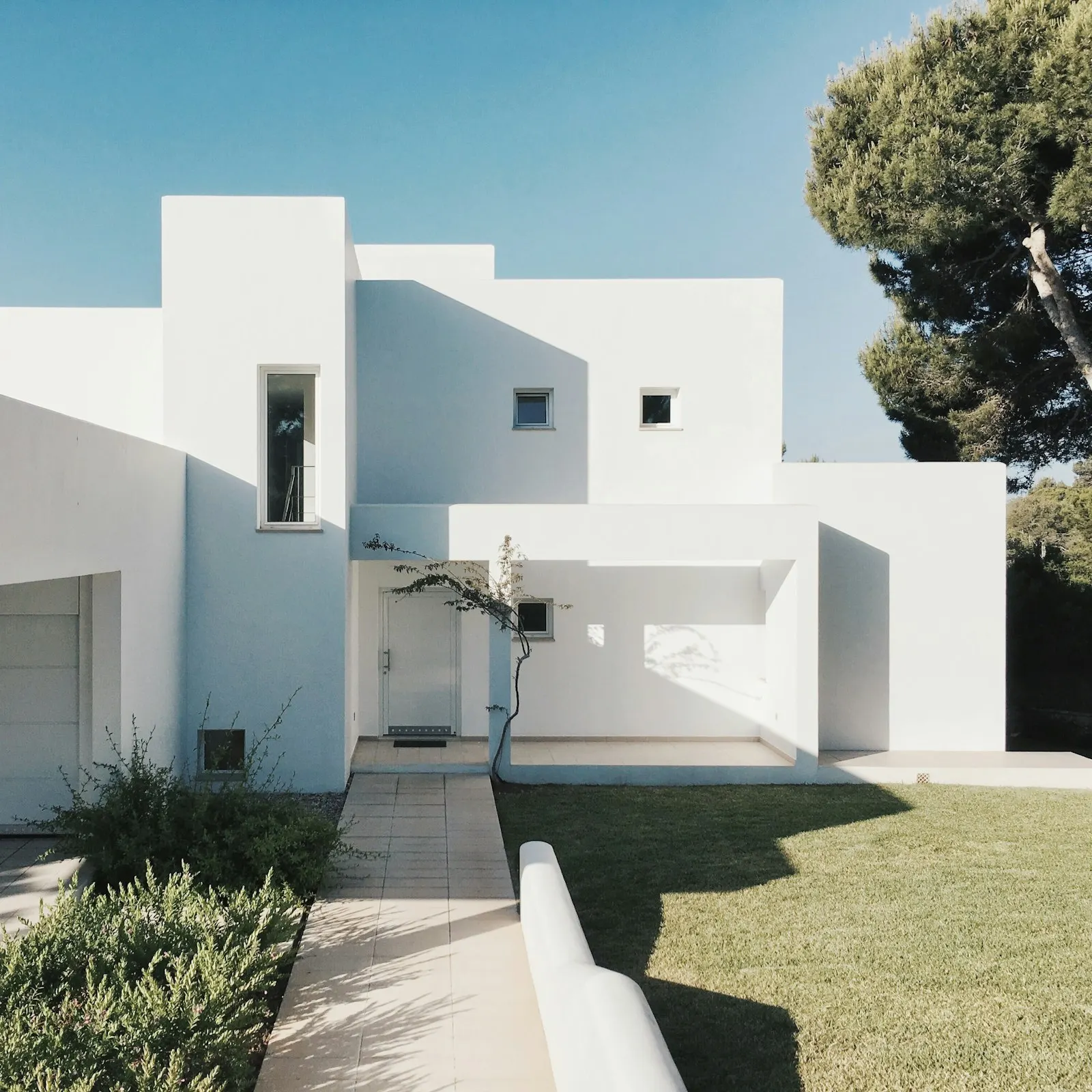 White cubic villa with deep-set windows and a stone path under a clear sky