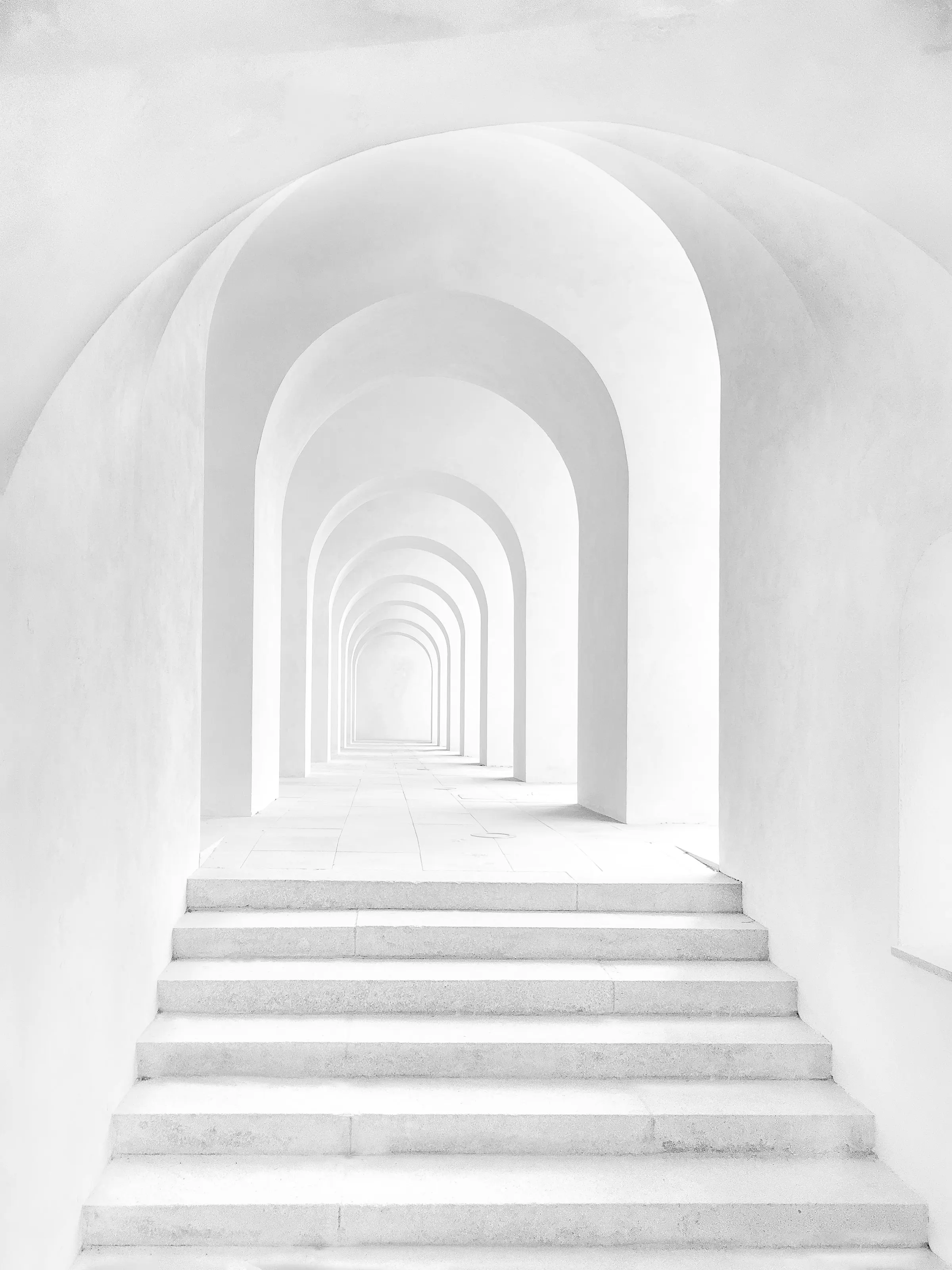 A white arcade of repeating arches receding into soft morning light