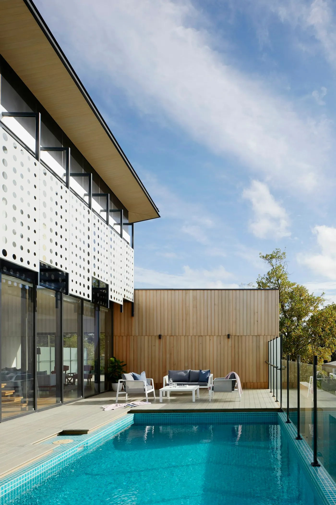 House with a perforated white screen facade and timber cladding beside a pool