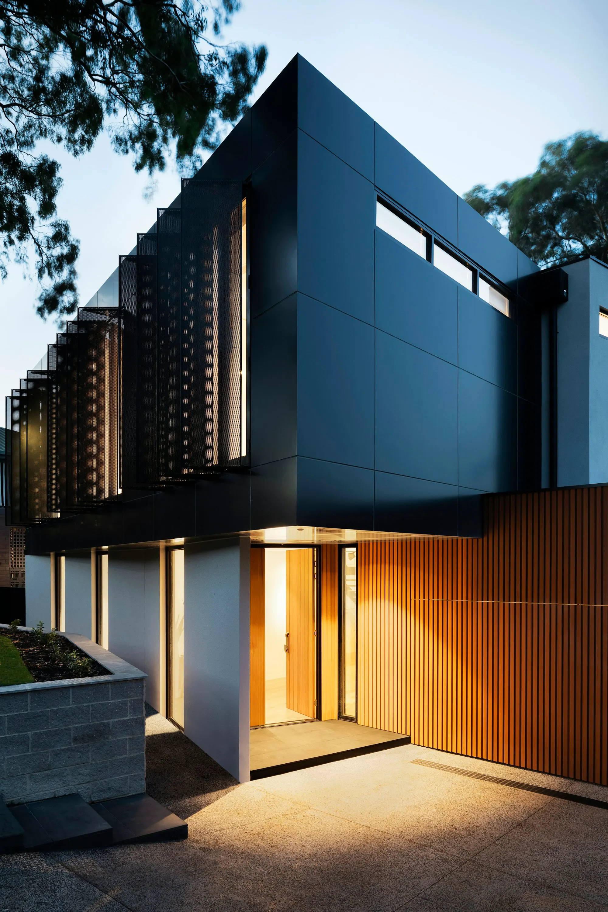 Dark facade with vertical timber fins, glowing warmly at dusk