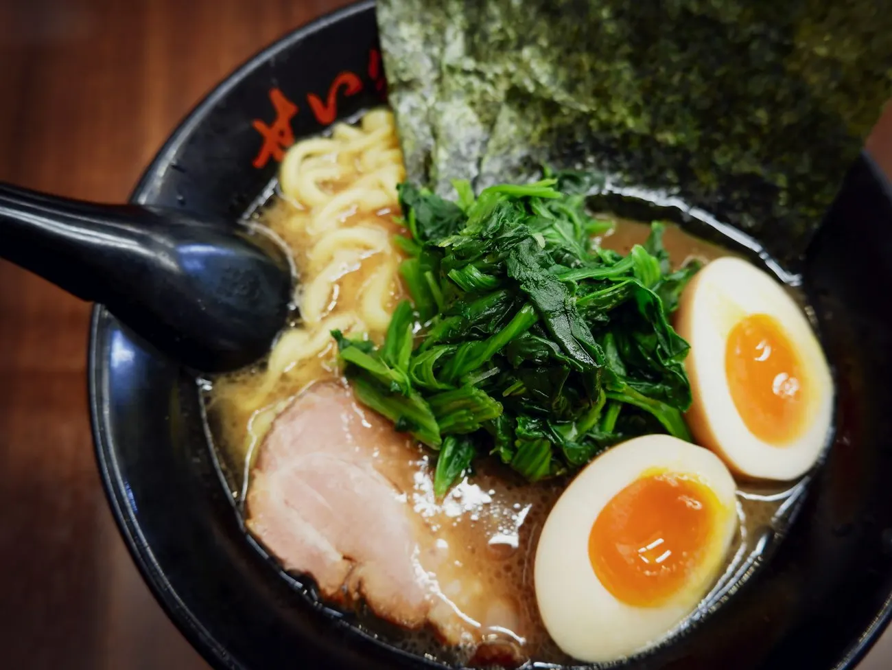 Tonkotsu ramen with chashu, soft egg, greens and nori in a black bowl