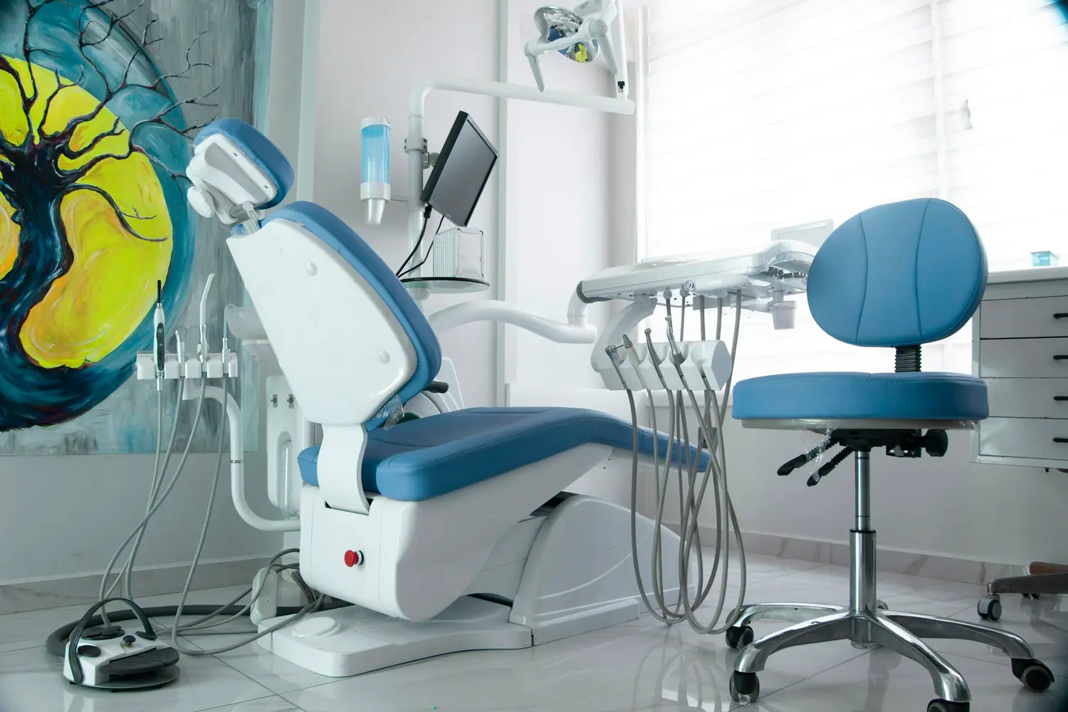 Behandlungszimmer mit blauem Behandlungsstuhl und Arzthocker